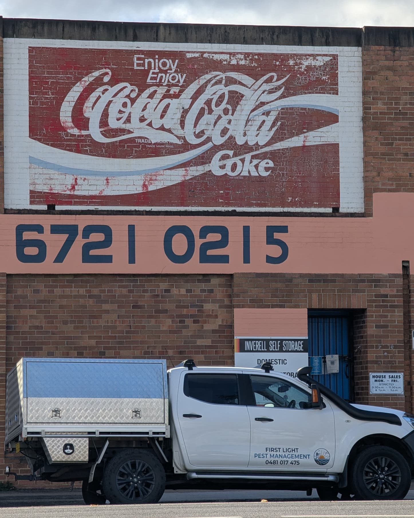 The First Light ute parked beneath a faded vintage Coca-Cola mural painted on a brick wall in Inverell